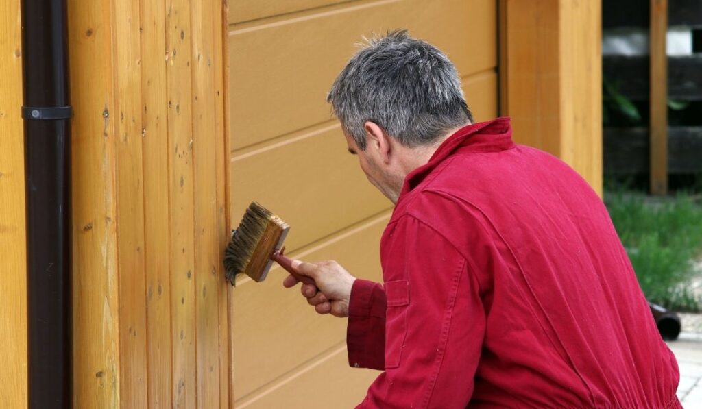 A man paints a garage with a wood preservative paint