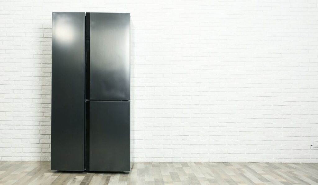 Modern refrigerator near white brick wall 