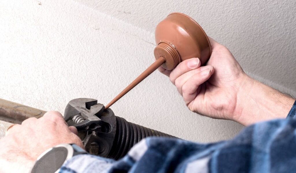 Preventative maintenance is being done by a handyman on the spring of a garage door