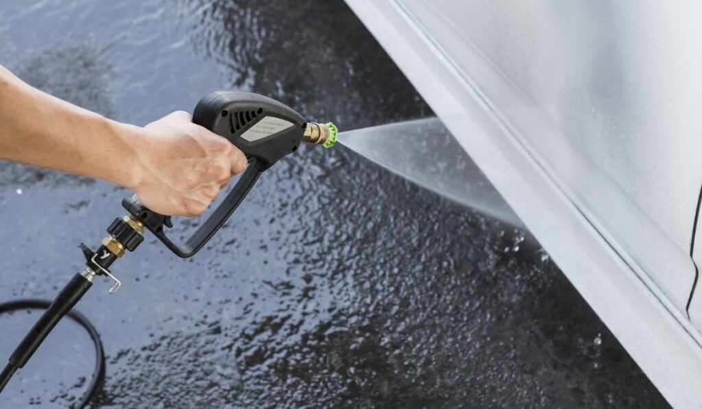 Washing the side skirt of a white car with a high pressure water spray gun 