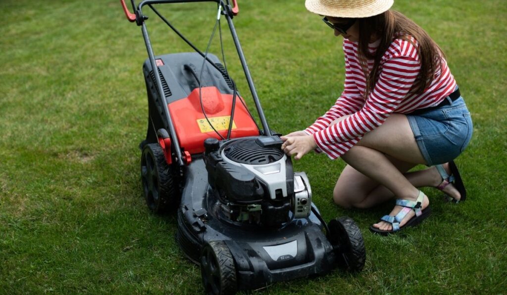 A girl removes the battery from a garden lawnmower