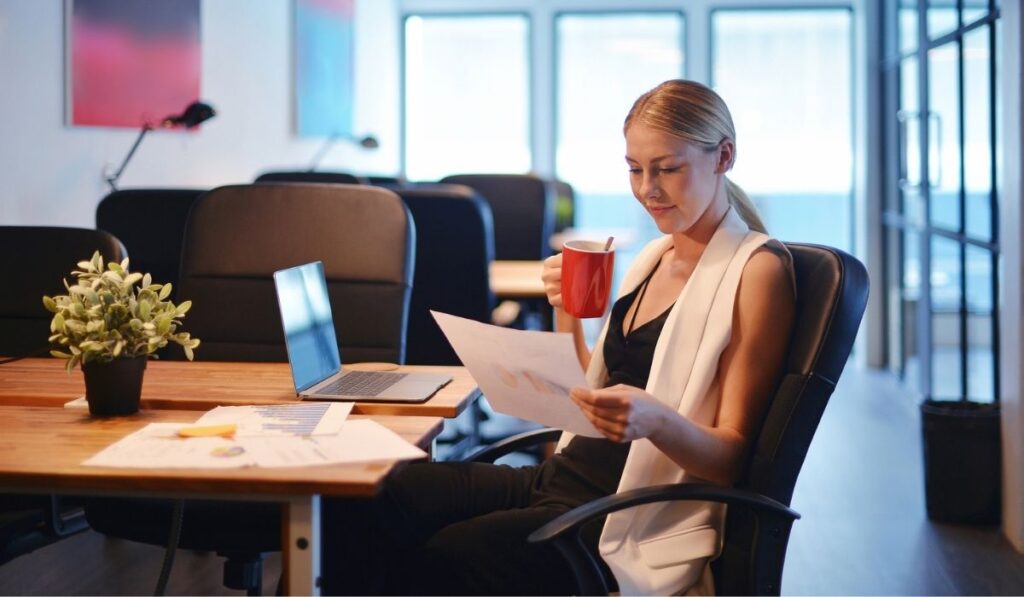 Business blonde girl drinking a cup of coffee and reading a business document 