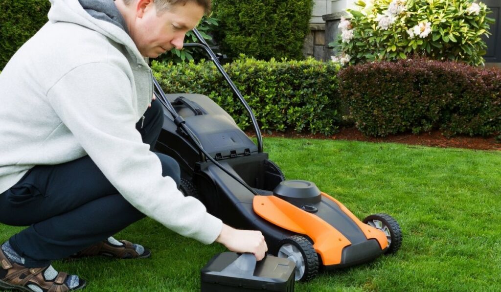 Mature man putting battery into electric Lawn Mower