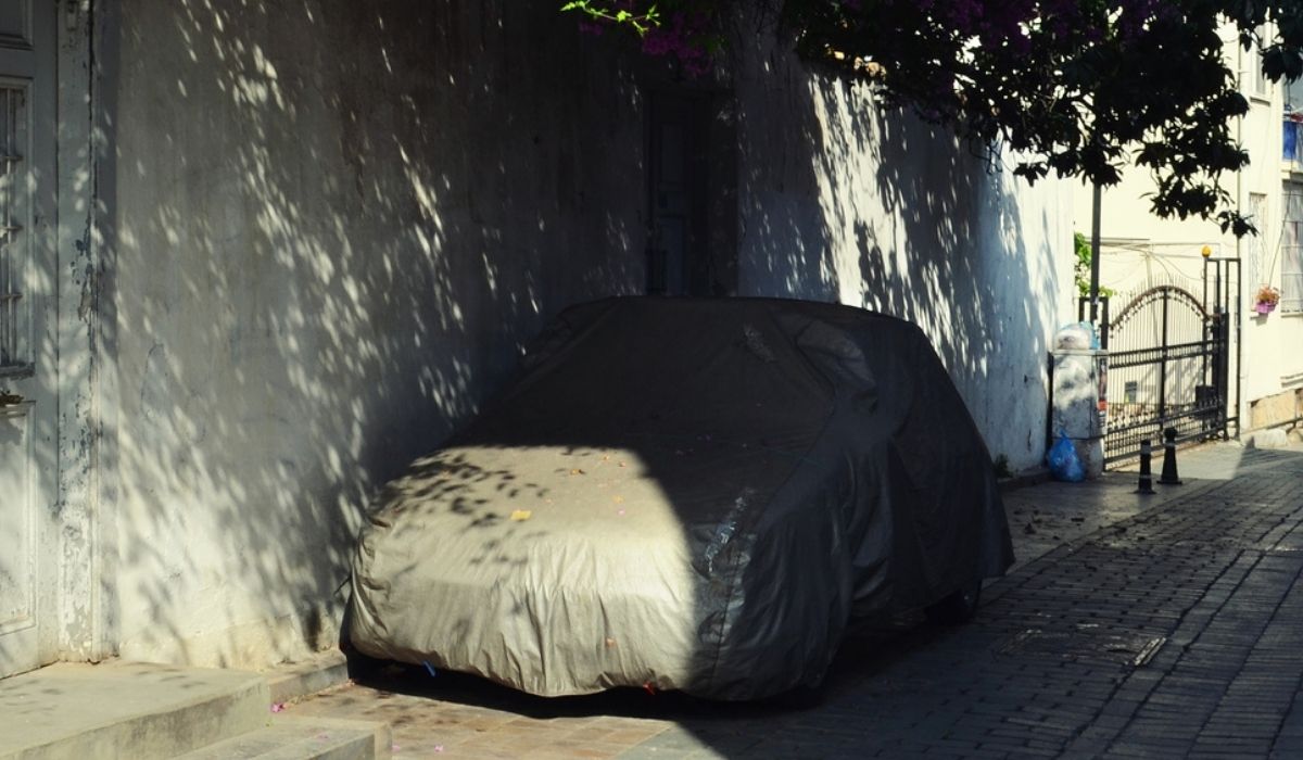 The car in a protective cover under shady home on a hot day