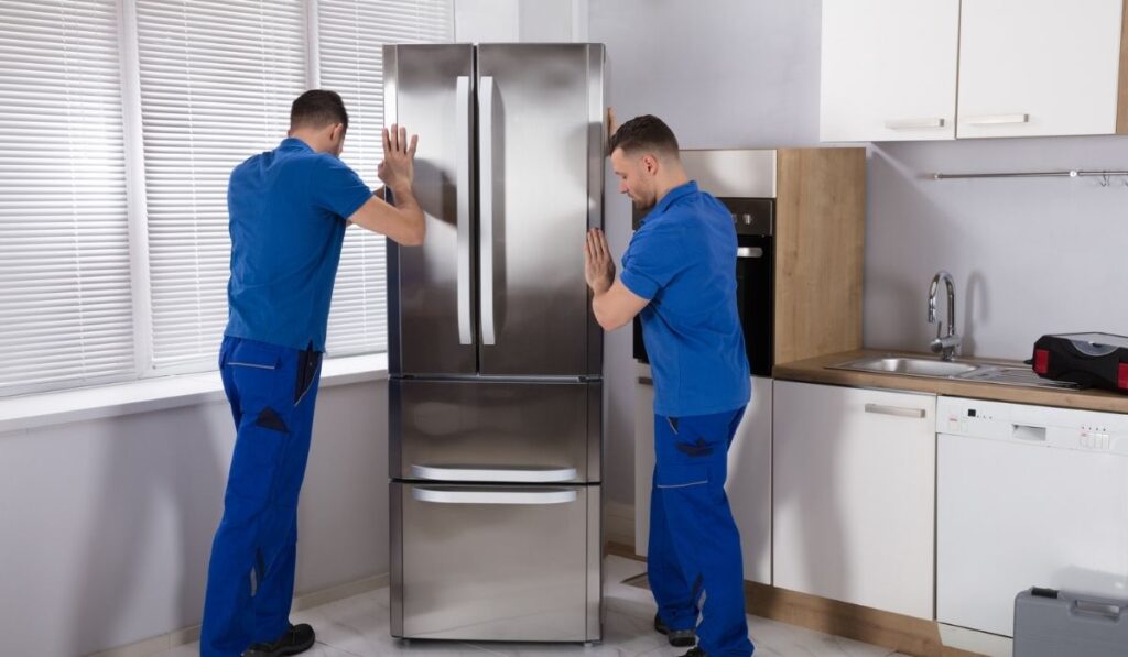 Two Movers Placing Refrigerator In Kitchen