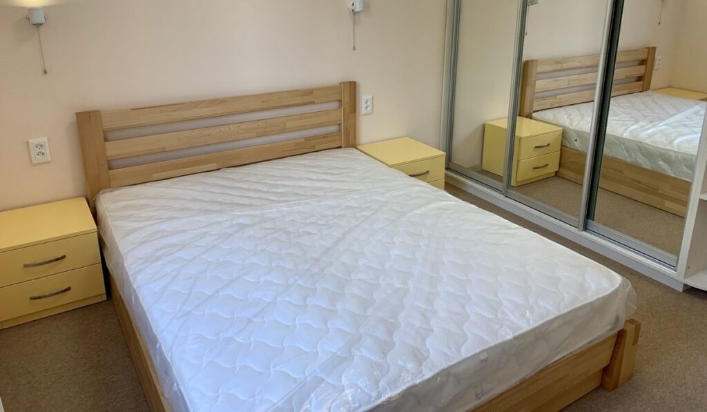 Wooden bed with white mattress with plastic