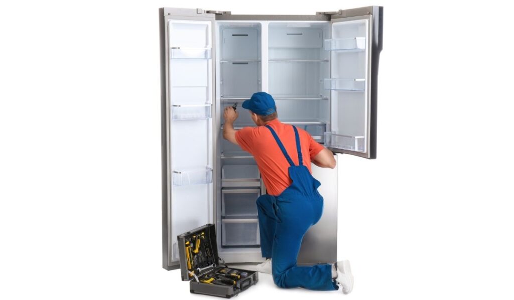 Male technician repairing refrigerator on background 