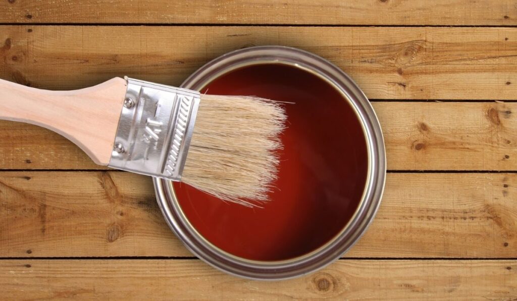 Red paint can with brush on wooden floor