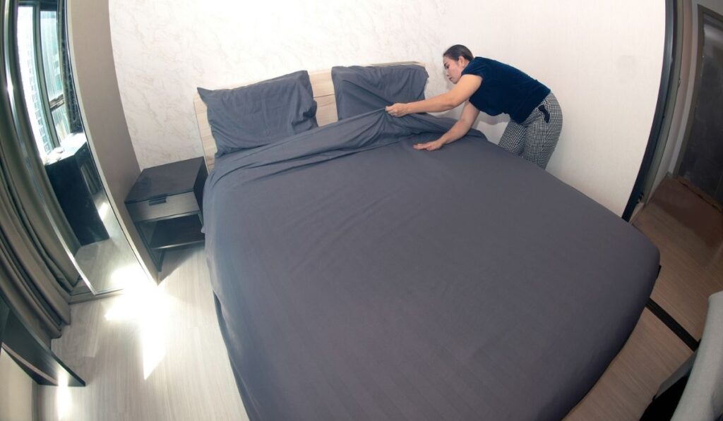 An Asian female maid making bed in hotel room