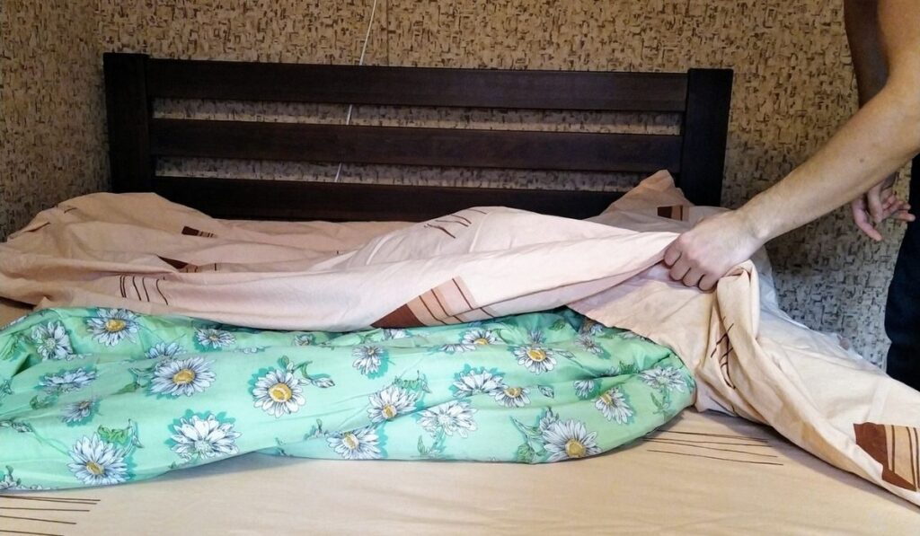 European man hold duvet cover over bed in bedroom