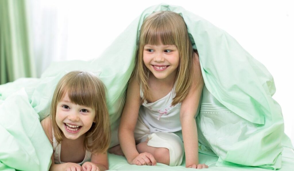 Little happy girls lying under blanket on bed 