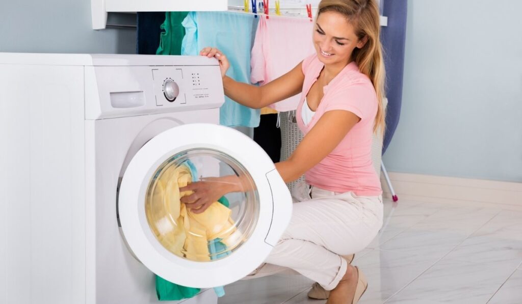 Smiling Woman Putting Clothes In Washing Machine