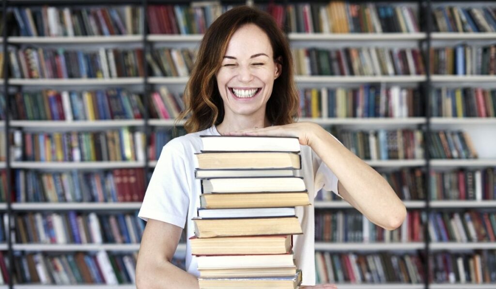 Woman model college student with books at library holds bunch of books 
