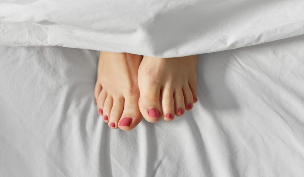 Feet of woman lying in bed under white blanket 