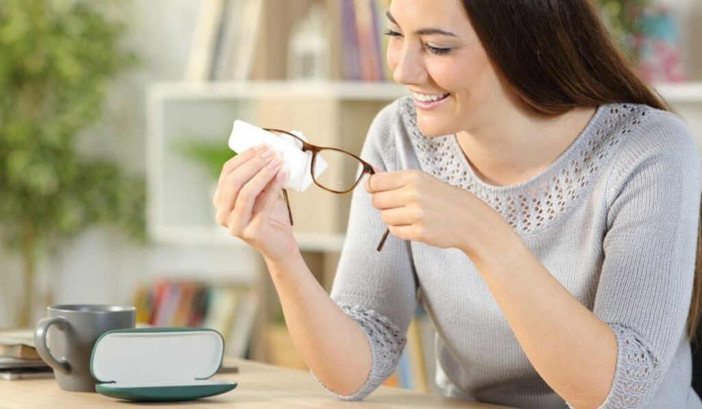 Happy woman cleaning eyeglasses with tissue at home 