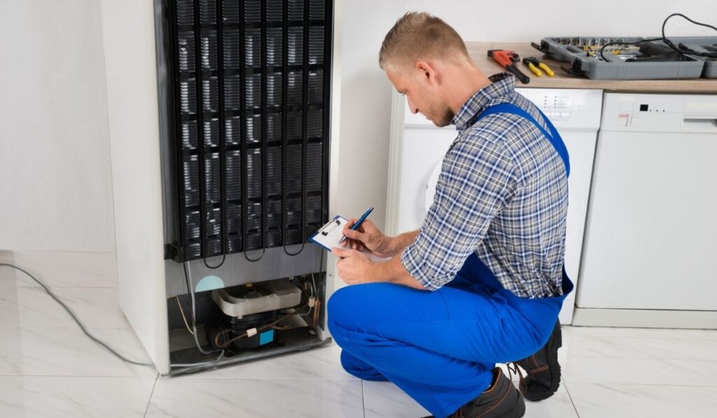 Plumber writing on clipboard in front of refrigerator 