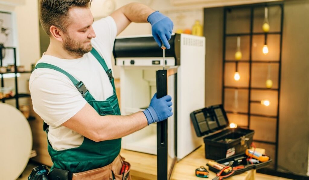 Worker with screwdriver repairs refrigerator door
