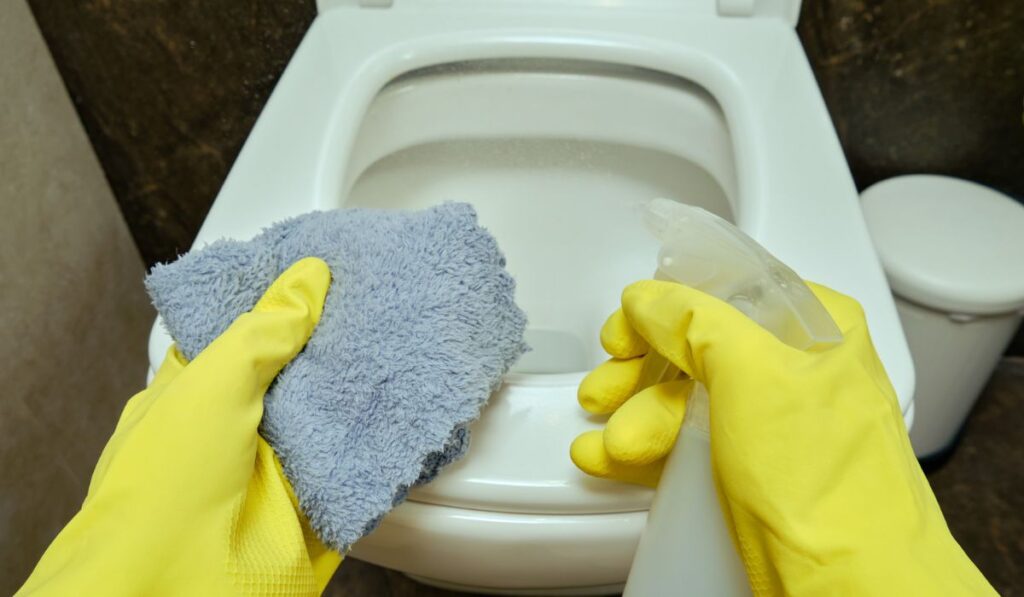 Man cleans up the bathroom by wiping the toilet bowl with a rag 