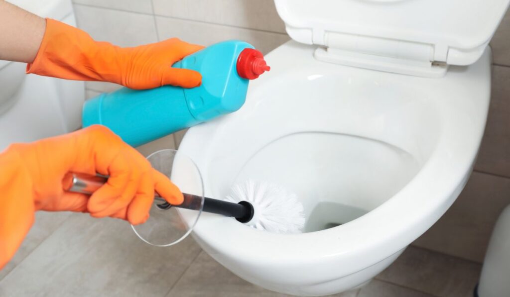 Woman in protective gloves cleaning toilet bowl with brush in bathroom