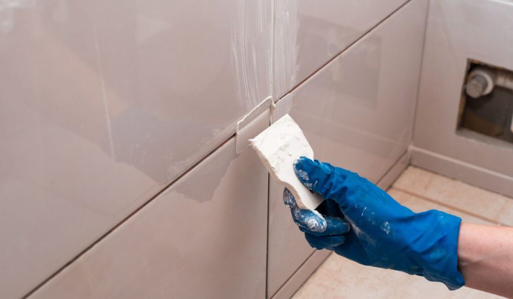 The master rubbing the tile joints with a white putty with a rubber spatula