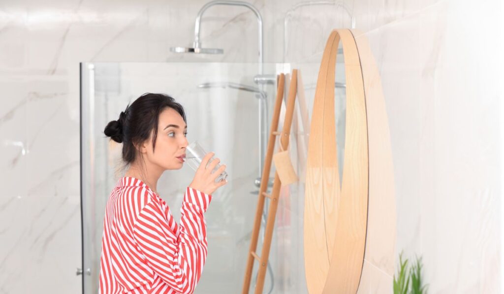 Young woman drinking water near mirror